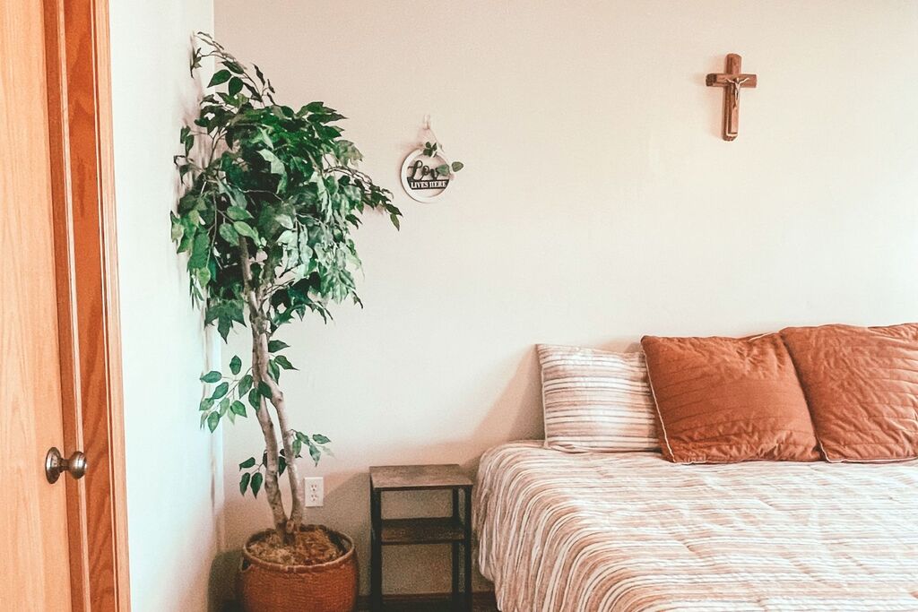 Bed with boho comforter brown accent pillows. Decorative tree, religious cross and rustic wood nightstand