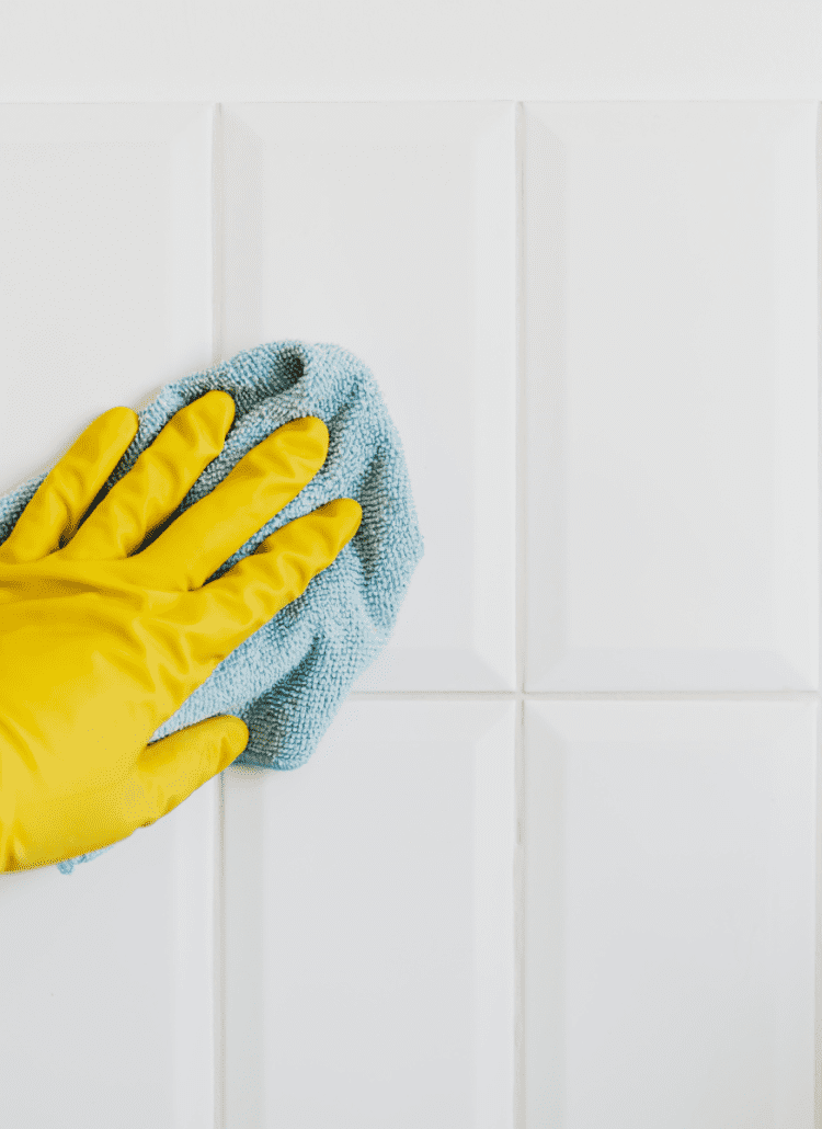 yellow cleaning glove with microfiber rag cleaning white subway tile wall